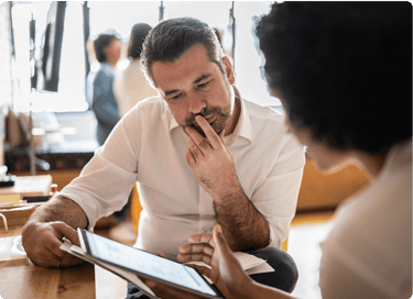 Man in white shirt listening thoughtfully to a colleague showing something on a digital tablet in an office.
