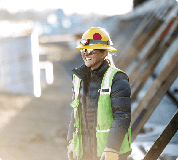 Smiling construction worker in safety gear and helmet standing at a worksite outdoors.
