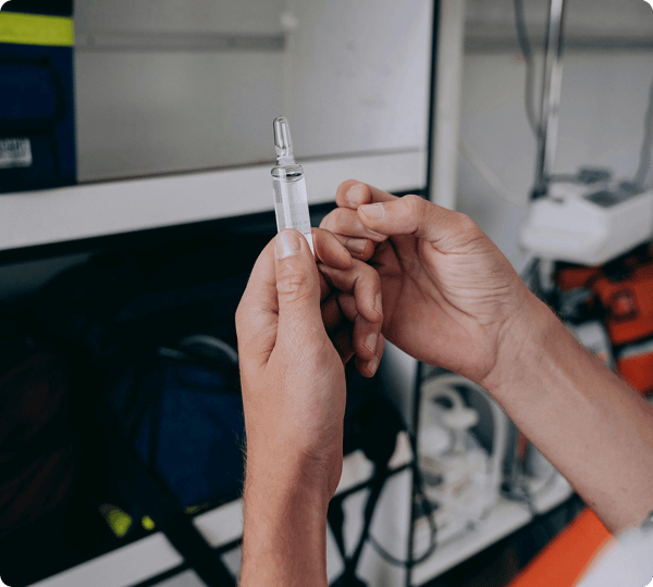 A person holds a small glass vial of clear liquid in a medical setting.