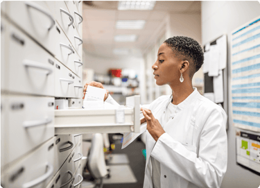 Pharmacist in a white coat organizing prescriptions in a drawer at a pharmacy.