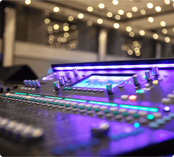 Close-up of a colorful audio mixing console with blurred lights in the background.