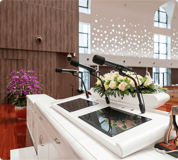 A podium with microphones, floral arrangement, and screens in a bright, modern auditorium.