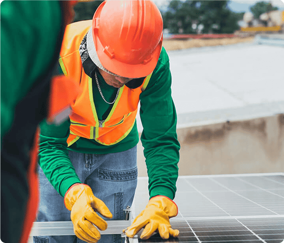 Worker in orange helmet and safety vest installing solar panels on a rooftop.