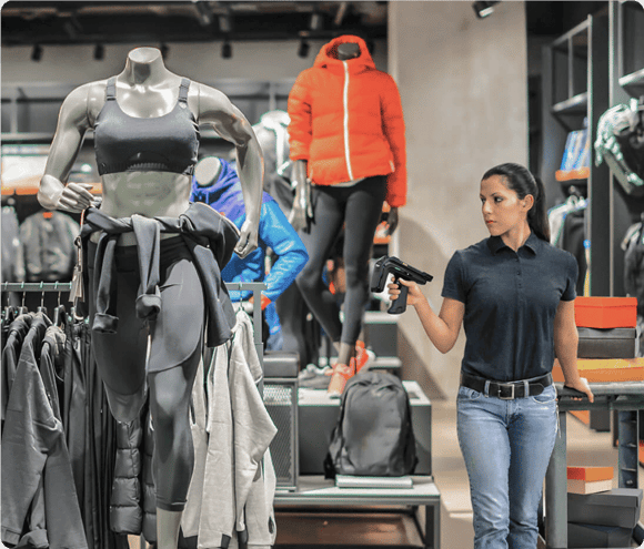 A woman holding a gun stands near mannequins dressed in sportswear inside a clothing store.